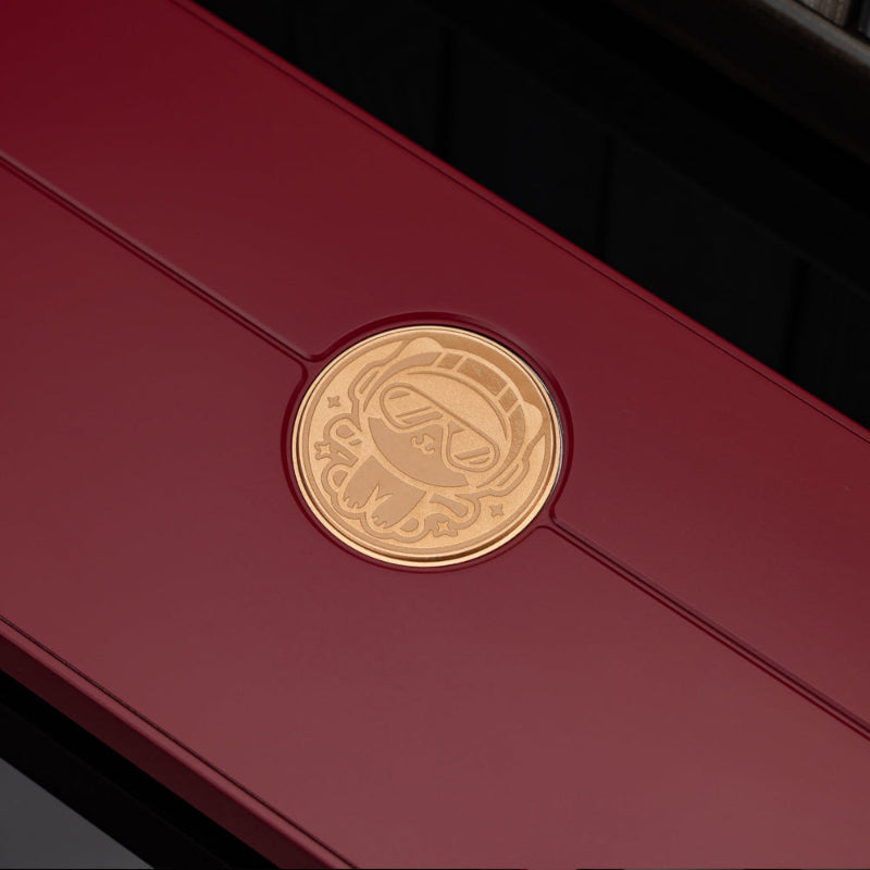 dark red rectangular box with a circular gold emblem featuring a stylized face